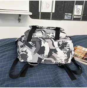 Nahaufnahme eines dunklen Graffiti-Schulrucksacks mit schwarzen Riemen auf einem Bett.