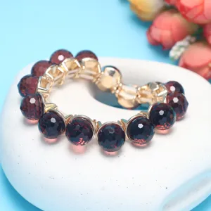 Detailed view of dark red faceted crystal bead bracelet with gold tone metal connectors on display.