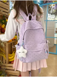 Detalle de una mochila escolar morada con patrones de corazones plateados y un dije de estrella