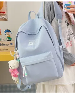 Dettaglio di uno zaino scolastico minimalista azzurro con un ciondolo a forma di orsetto.