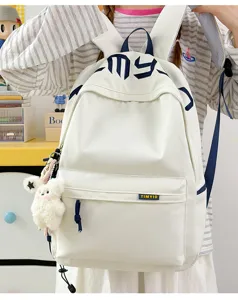 Detail view of a white student backpack featuring blue embroidery and a plush bear keychain.