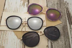 A lifestyle close-up showing three styles of trendy round sunglasses on a wooden desk.