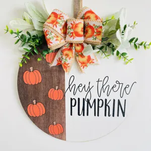 Round wooden fall door sign featuring a pumpkin pattern, bow, and greenery decor for autumn.