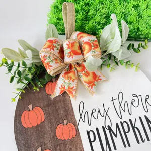 Detailed view of fall wooden pumpkin door sign with bow and green leaves, seasonal decor.