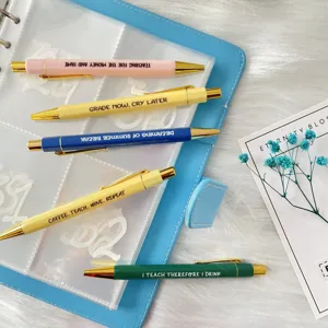 Close-up detail of colorful teacher ballpoint pens set with English funny quotes and gold trim.