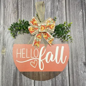 Detailed close-up of autumn wooden door sign featuring a pumpkin bow and fall leaves.