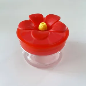 Handheld hummingbird feeder with red flower lid and clear base for outdoor garden use.