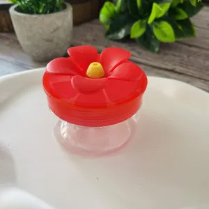 Handheld plastic hummingbird feeder with red flower lid for garden outdoor feeding detail view.