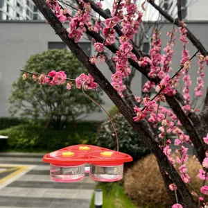 Outdoor hanging hummingbird feeder detail view showing red base clear nectar cups and flower ports.