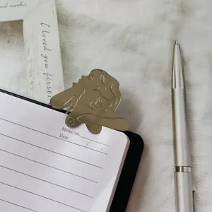 Gros plan détaillé du marque-page en métal doré en forme de femme sur un carnet.