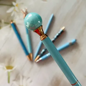 Close-up detail shot of light blue ballpoint pen featuring pearl top and gold metal accents.