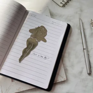 Vue détaillée du marque-page femme ton or posé sur un carnet. Article de papeterie en métal.