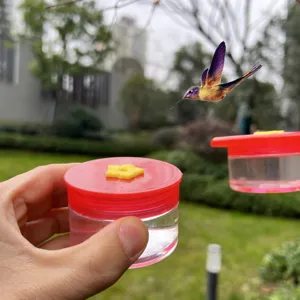 Handheld hummingbird feeder with bright red lid and yellow flower port for outdoor garden use.