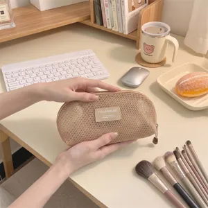 Minimalist beige mesh makeup brush bag with shell design held in hands for detail view.
