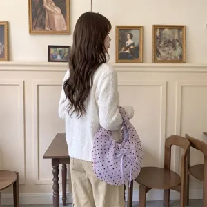 Detalle de un bolso de organza lavanda con lunares, un lazo decorativo y diseño plisado