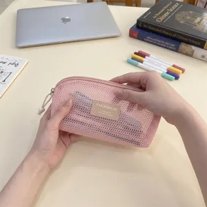 Detailed view of a pink mesh makeup and stationary pouch held by hands in a study setting