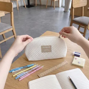 Detail view of white mesh shell storage bag being opened on a wooden desk with pens