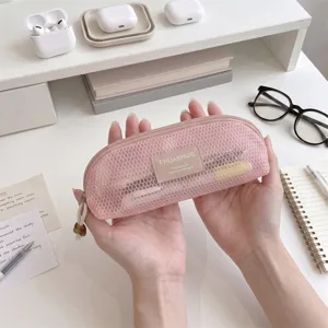 Detailed view of a pink mesh makeup brush pouch held by hands in a lifestyle desk setting