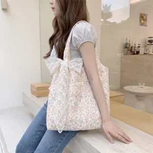 A detailed lifestyle shot of a large floral canvas tote bag featuring a white decorative lace bow.