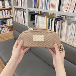 Close-up of a beige mesh shell-shaped pencil case with a cute heart charm in a library.