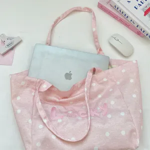 Detailed lifestyle view of pink polka dot tote bag with Lucky embroidery and laptop