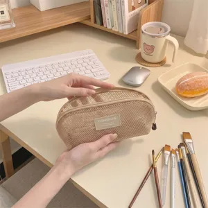 Close-up of a portable beige mesh shell-shaped cosmetic pouch being opened on a desk.