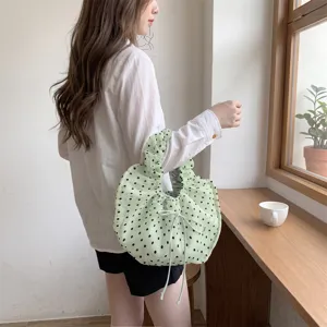 Detalle de bolso de organza verde claro con lunares sostenido por modelo en una cafetería.