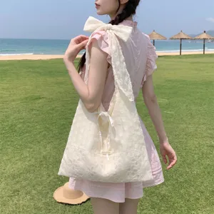 Detalle del bolso tote de organza crema con lazo en una playa soleada y relajada