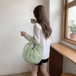 Detalle de una modelo que lleva un bolso de organza verde con lunares y un lazo.