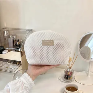 Weiße Netz-Kosmetiktasche in Muschelform, gehalten vor einem hellen Schminktisch