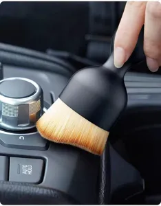 Soft bristle car detailing brush close-up showing fine cleaning action on air vent and console gaps.