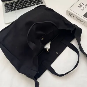 Vista detallada del bolso tote de lona negra con correa ancha para el hombro e interior