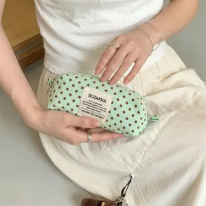 Close-up of a stylish mint green canvas pouch with brown polka dots held by a model