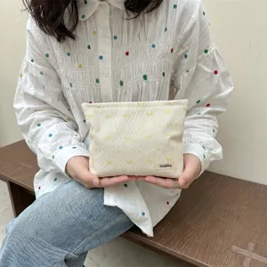 Close-up of a girl holding a cream-colored bow pattern embroidery makeup pouch in her hands