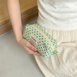 Close-up view of a mint green canvas polka dot makeup bag held by a person wearing white