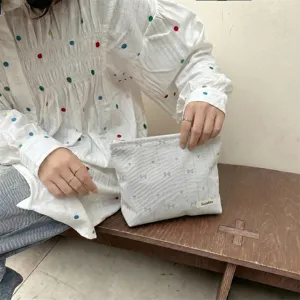 Detail of a hand-held makeup bag with bow and heart embroidery in a lifestyle setting.