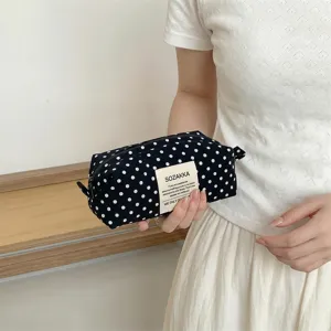 Close-up of a navy blue polka dot canvas makeup bag held by hand in a minimalist setting