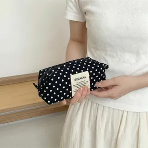 Close-up of a black canvas polka dot makeup bag with brand label held by hands