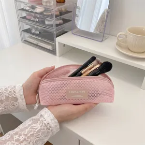Detailed view of pink mesh makeup brush bag held in hands with various brushes inside.