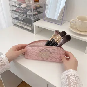 Detailed view of pink mesh makeup brush storage bag being held on a vanity desk.