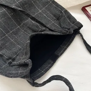 Detail of a dark grey plaid drawstring bag showing fabric texture and black interior.