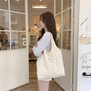 Modell trägt eine große minimalistische cremefarbene Segeltuchtasche in einem Shop.