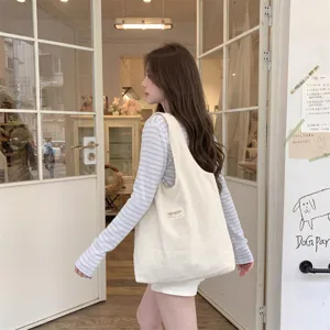 Große beige Segeltuch-Tragetasche, von einem Model für einen lässigen Look getragen