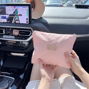 Detail van een draagbaar roze opbergtasje met rits voor cosmetica, vastgehouden in auto.