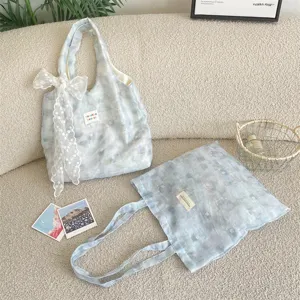 Ice blue mottled floral tote bag with lace bow accessory on a beige textured sofa