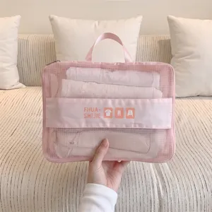 Close-up of a pink mesh travel organizer bag held by hand, showing internal clothes.