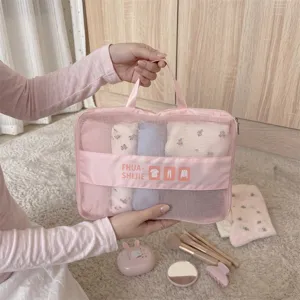 Handheld pink mesh travel storage bag organizer filled with clothes and beauty accessories