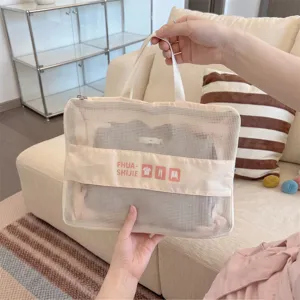 Close-up of a hand holding a cream-colored mesh travel storage bag for clothing organization
