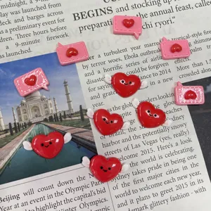 Detailed close-up of cute red winged heart and pink speech bubble resin cabochons for crafts.