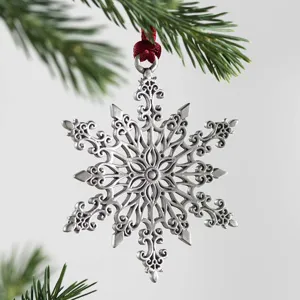 Close-up of a detailed silver filigree snowflake Christmas tree ornament hanging on pine.